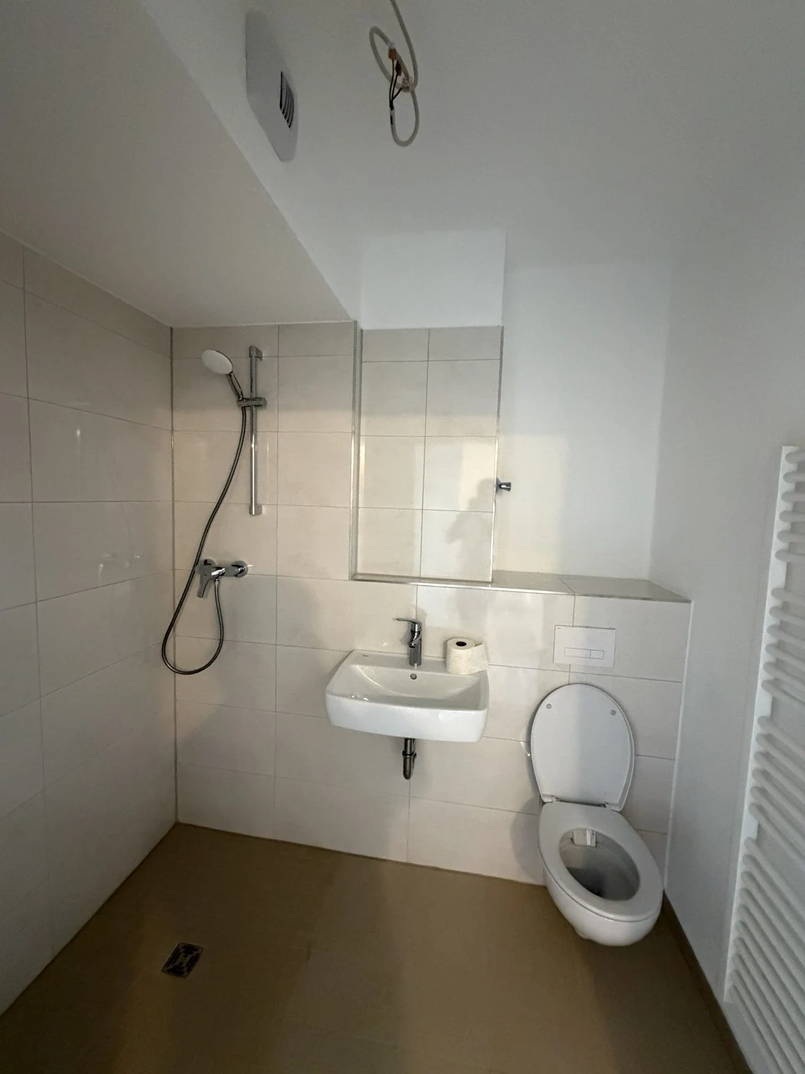 Innenausbau eines Badezimmers mit gefliestem Duschbereich, Waschtisch und WC